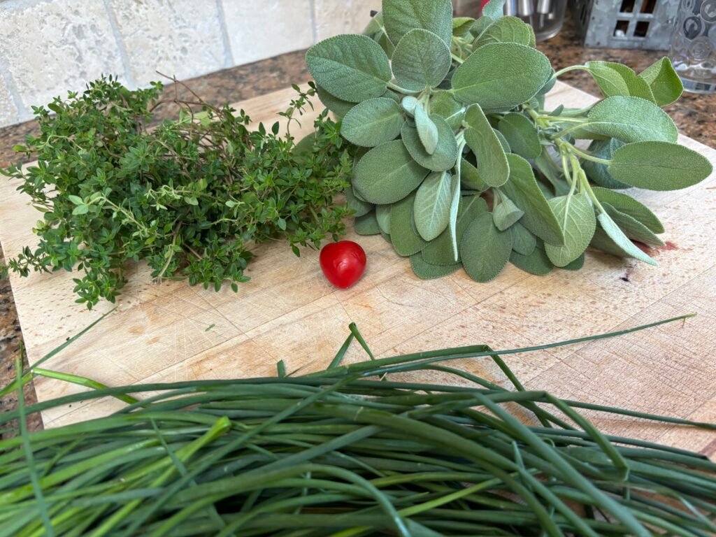 Fresh herbs from my garden on a wooden board including sage, thyme, and chives, representing clean, intentional living